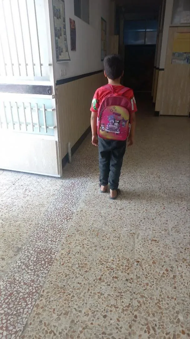A young boy, seen from behind, walking down a school hallway wearing his new backpack